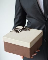 Unrecognizable businessman holding brown gift box and pointing with forefinger at it. Sales manager presenting Christmas present. Holiday shopping sale concept