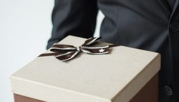 Unrecognizable businessman holding brown gift box and pointing with forefinger at it. Sales manager presenting Christmas present. Holiday shopping sale concept